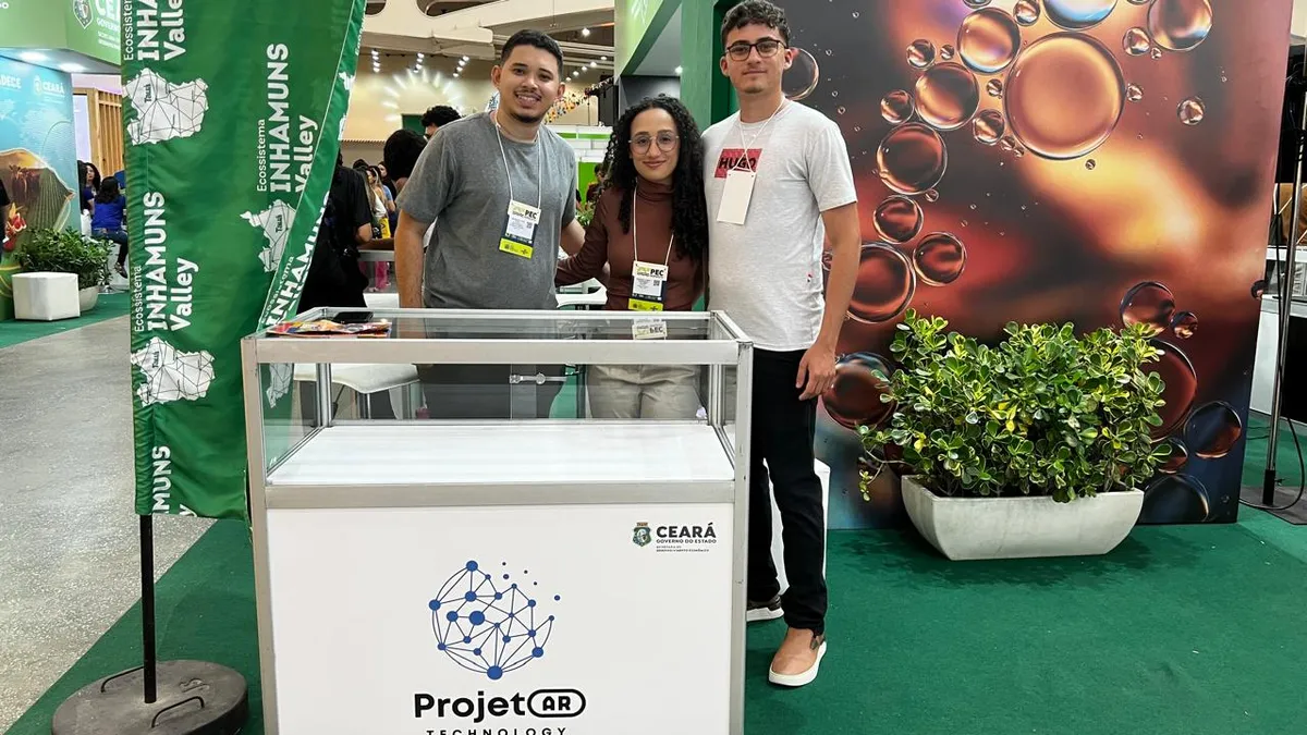 Três integrantes da Projetar no estande do Inhamuns Valley, ao lado de um balcão com o logo da ProjetAR